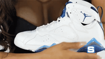 A Woman Is Holding A White And Blue Air Jordan Shoe GIF