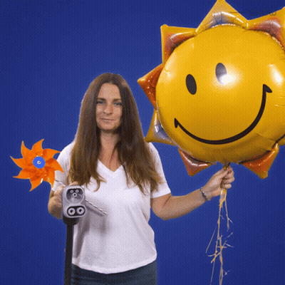 A Woman Is Holding A Windmill And A Balloon With A Smiley Face On It GIF