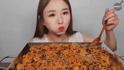 A Woman Is Holding A Wooden Spoon Over A Pan Of Food With The Name Hamzy On The Bottom GIF