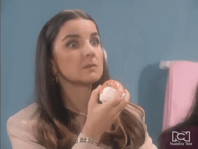 A Woman Is Holding An Apple In Her Hand In Front Of Her Face . GIF