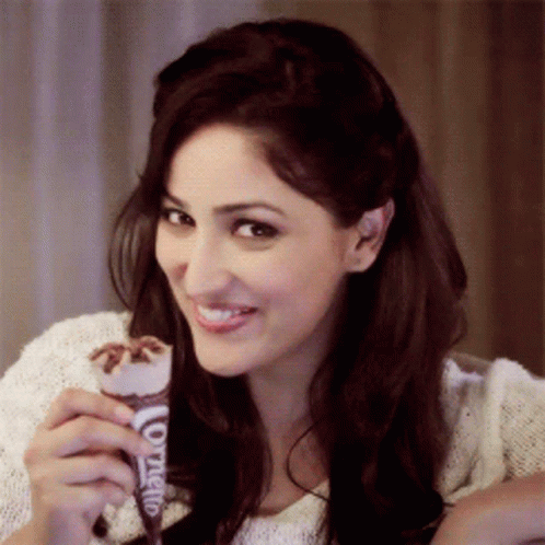 A Woman Is Holding An Ice Cream Cone That Says Cornetto On It GIF
