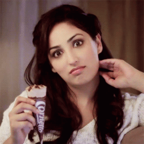 A Woman Is Holding An Ice Cream Cone That Says Cornetto On It GIF