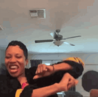 A Woman Is Holding Another Woman 'S Arm In A Room With A Ceiling Fan . GIF