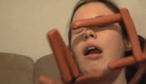 A Woman Is Holding Three Hot Dogs In Front Of Her Face . GIF