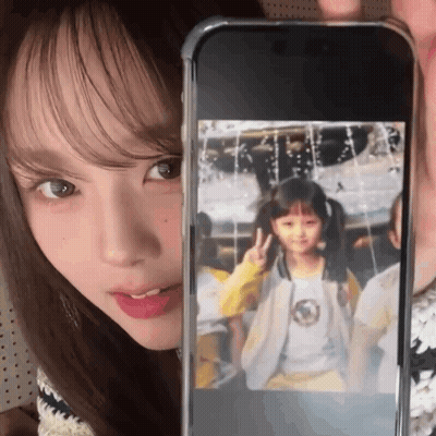 A Woman Is Holding Up A Cell Phone With A Picture Of A Young Girl On It GIF