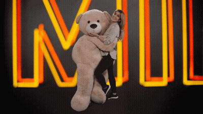 A Woman Is Hugging A Giant Teddy Bear In Front Of A Neon Sign That Says Lnwl GIF