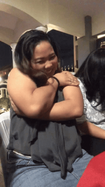 A Woman Is Hugging Another Woman In A Dark Room At Night GIF