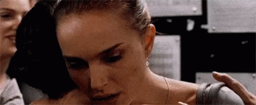 A Woman Is Hugging Another Woman In A Room While A Man Holds Her Shoulder . GIF