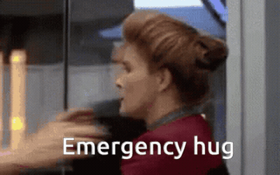 A Woman Is Hugging Another Woman With The Words `` Emergency Hug '' Written On The Bottom Of The Image . GIF