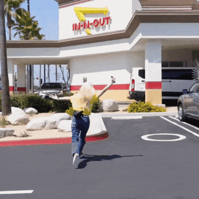 A Woman Is Jumping In Front Of An In N Out Restaurant GIF