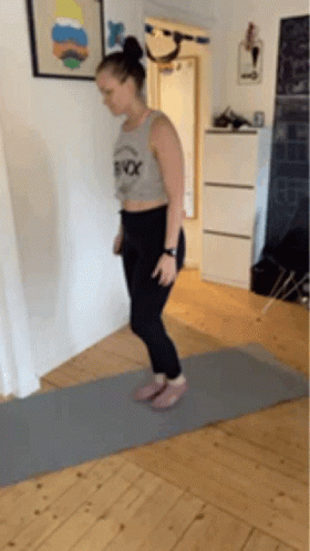 A Woman Is Jumping On A Yoga Mat In A Hallway . GIF
