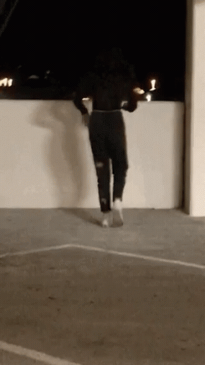 A Woman Is Jumping Over A Wall In A Parking Lot . GIF