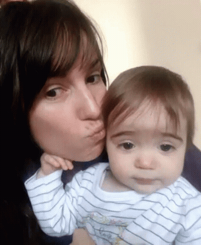 A Woman Is Kissing A Baby On The Cheek And The Baby Is Wearing A Striped Shirt GIF