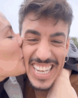 A Woman Is Kissing A Man On The Cheek While Smiling . GIF