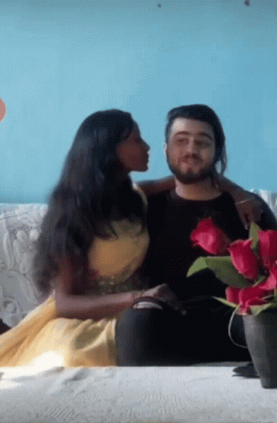 A Woman Is Kissing A Man On The Cheek While They Sit On A Couch GIF