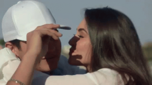 A Woman Is Kissing A Man On The Forehead While He Is Wearing A White Hat . GIF