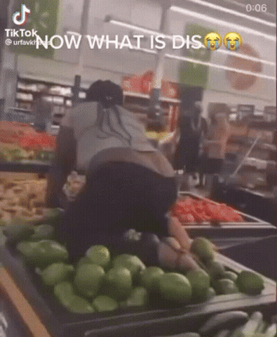 A Woman Is Kneeling Down In Front Of A Tray Of Green Peppers . GIF