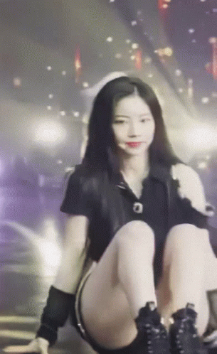 A Woman Is Kneeling Down On A Stage With Her Legs Crossed And Looking At The Camera . GIF