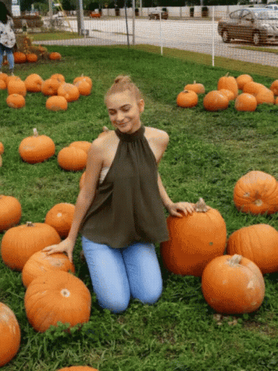 A Woman Is Kneeling In A Field Of Pumpkins And Smiling GIF