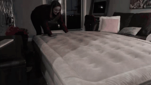 A Woman Is Kneeling On A Mattress In A Dark Room GIF