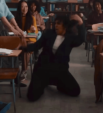 A Woman Is Kneeling On The Floor In A Classroom With Other People GIF