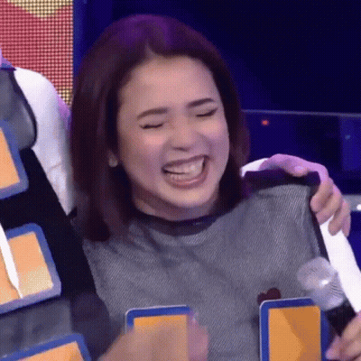 A Woman Is Laughing And Holding A Microphone While Sitting On A Stage . GIF