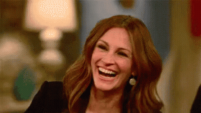 A Woman Is Laughing And Smiling While Sitting At A Table . GIF
