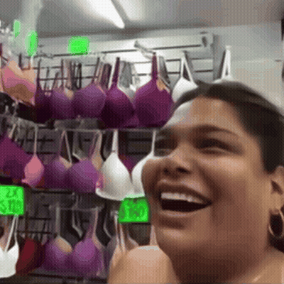 A Woman Is Laughing In Front Of A Display Of Purple And White Bras GIF