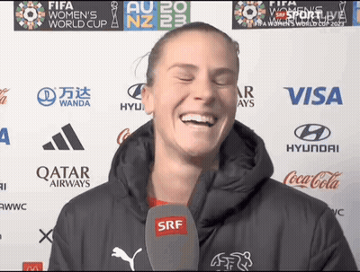 A Woman Is Laughing In Front Of A Wall With Logos For Qatar Airways Coca Cola And Visa GIF