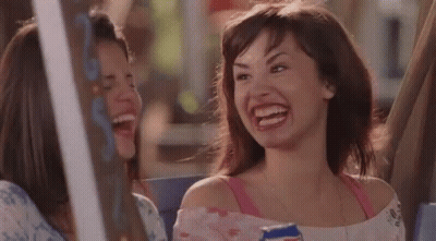 A Woman Is Laughing While Holding A Can Of Soda And Sitting Next To Another Woman . GIF