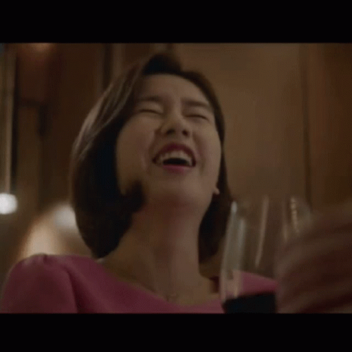 A Woman Is Laughing While Holding A Glass Of Wine In Her Hand . GIF