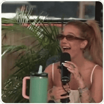 A Woman Is Laughing While Holding A Microphone In Front Of A Green Cup . GIF