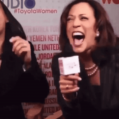 A Woman Is Laughing While Holding A Microphone In Front Of A Toyota Women Sign GIF