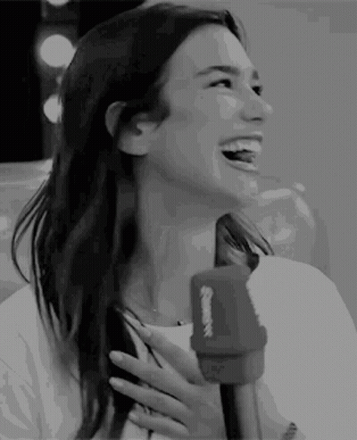 A Woman Is Laughing While Holding A Microphone In Her Hand . GIF