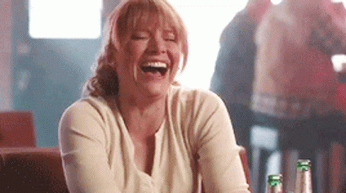 A Woman Is Laughing While Sitting At A Table In A Bar . GIF