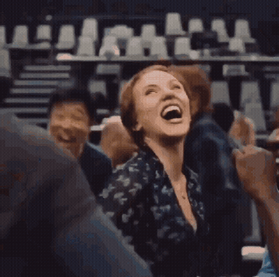 A Woman Is Laughing While Sitting In A Crowd Of People In A Theater . GIF