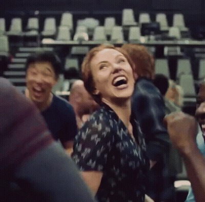 A Woman Is Laughing While Sitting In A Crowd Of People . GIF
