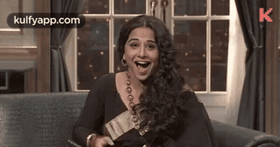 A Woman Is Laughing While Sitting On A Couch . GIF