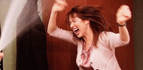 A Woman Is Laughing With Her Arms In The Air While Standing In Front Of A Door . GIF