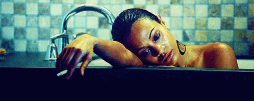 A Woman Is Laying In A Bathtub Smoking A Cigarette And Looking At The Camera . GIF