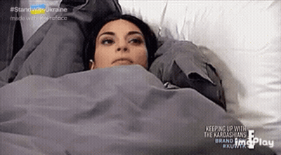 A Woman Is Laying In A Bed Under A Blanket And Looking Up . GIF