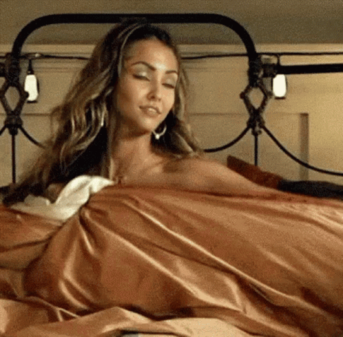 A Woman Is Laying In A Bed With A Blanket On Her GIF