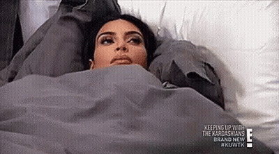 A Woman Is Laying In A Bed With A Blanket On Her Head . GIF