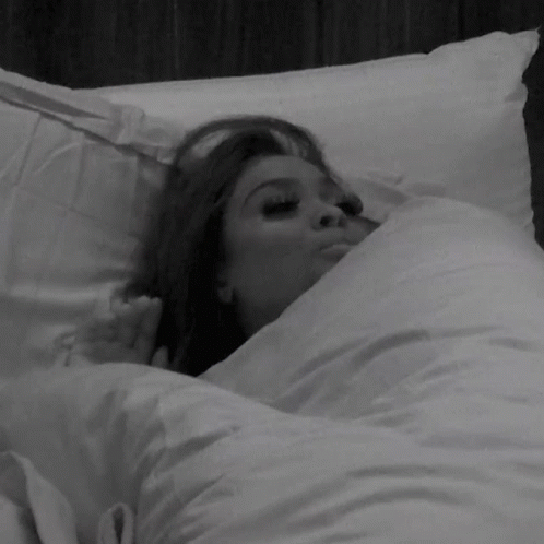 A Woman Is Laying In A Bed With White Sheets GIF