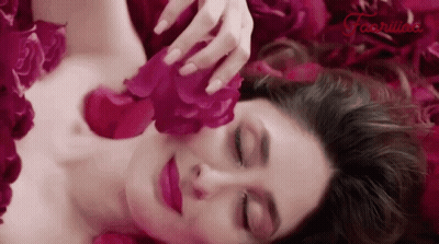 A Woman Is Laying In A Pile Of Pink Rose Petals GIF