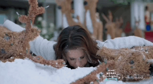 A Woman Is Laying In A Pile Of Stuffed Reindeer With The Words Merry Thanksgiving Written On The Bottom GIF