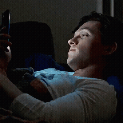 A Woman Is Laying In Bed Looking At Her Phone And Smiling . GIF