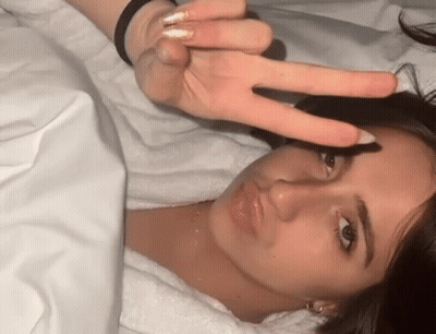 A Woman Is Laying In Bed Making A Peace Sign With Her Finger . GIF