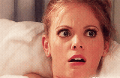A Woman Is Laying In Bed Making A Surprised Face . GIF