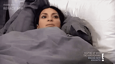 A Woman Is Laying In Bed Under A Blanket With Her Head On A Pillow . GIF